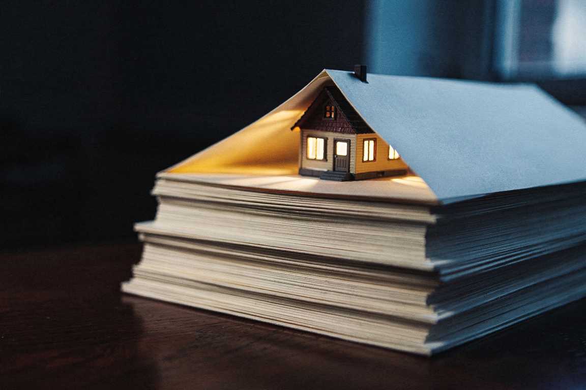 A miniature house with warmly lit windows, sheltered under a tent of blank pages